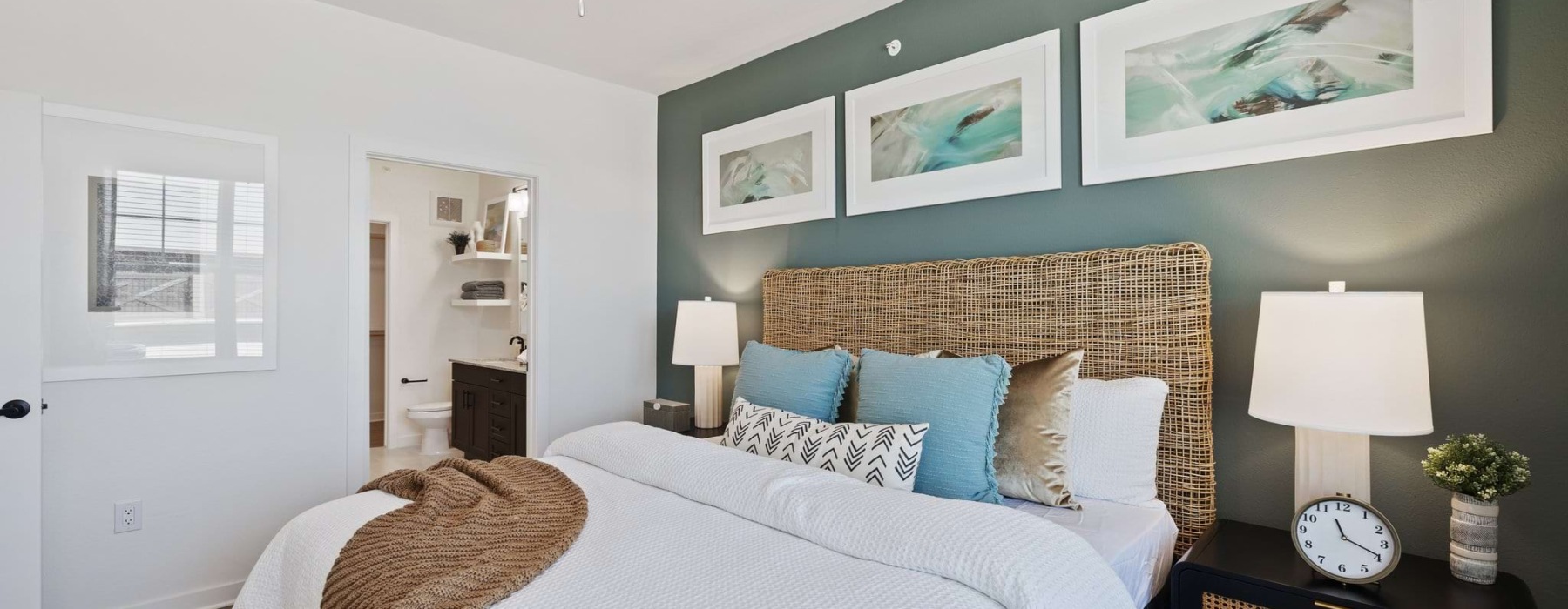 Model bedroom at Silos Harvest Green Apartments in Richmond, TX, featuring a bedside table and a view of the bathroom.
