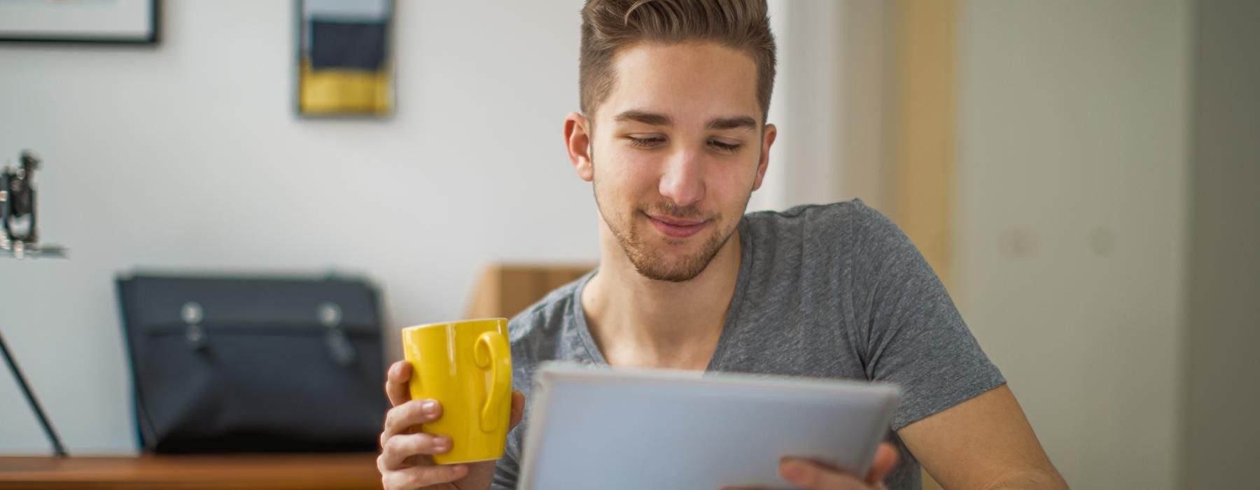 man holding a coffee cup and looking at a laptop